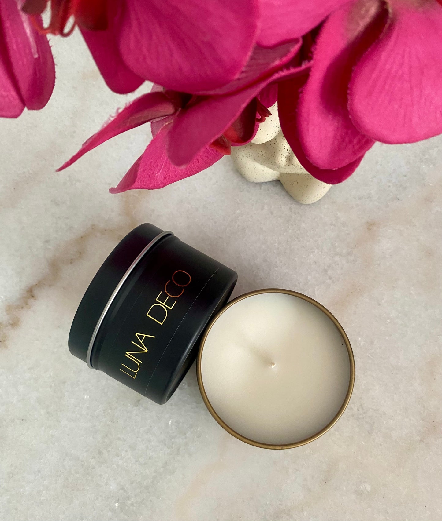 Open candle with 'Luna Deco' branding next to pink flowers on a textured surface.
Matte black travel tin candle,  perfect for travel, small spaces or thoughtful gifting.
Minimalist, timeless, elegant design, artisan-made candles. 
Luna Deco. 