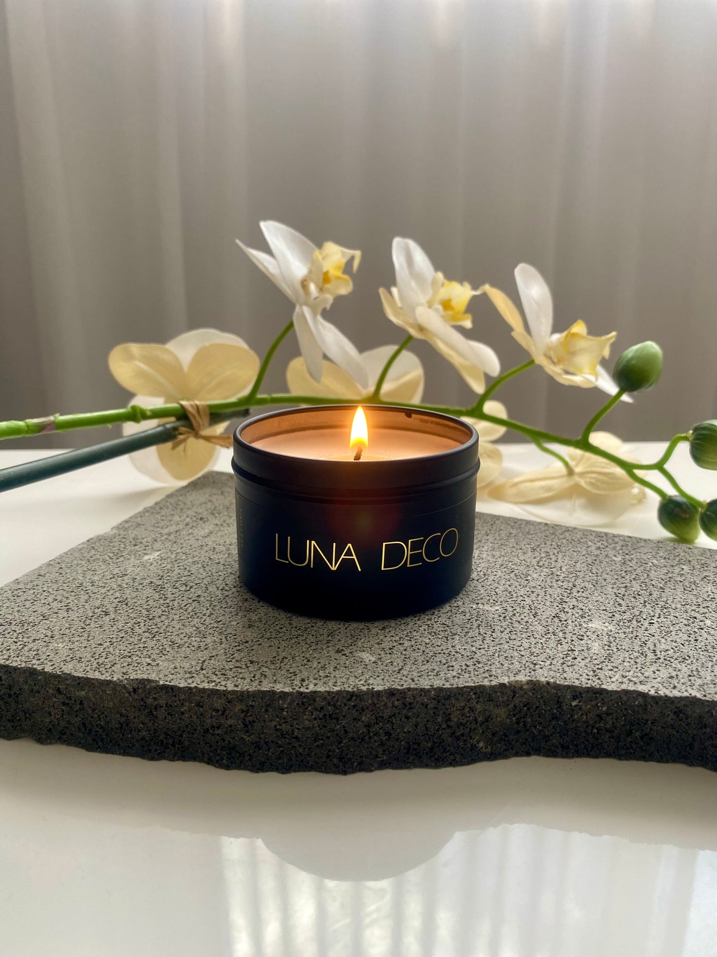 Luna Deco black travel tin candle in a black container with white flowers in the background.
Matte black travel tin candle,  perfect for travel, small spaces or thoughtful gifting.
Minimalist, timeless, elegant design, artisan-made candles. 
Luna Deco. 