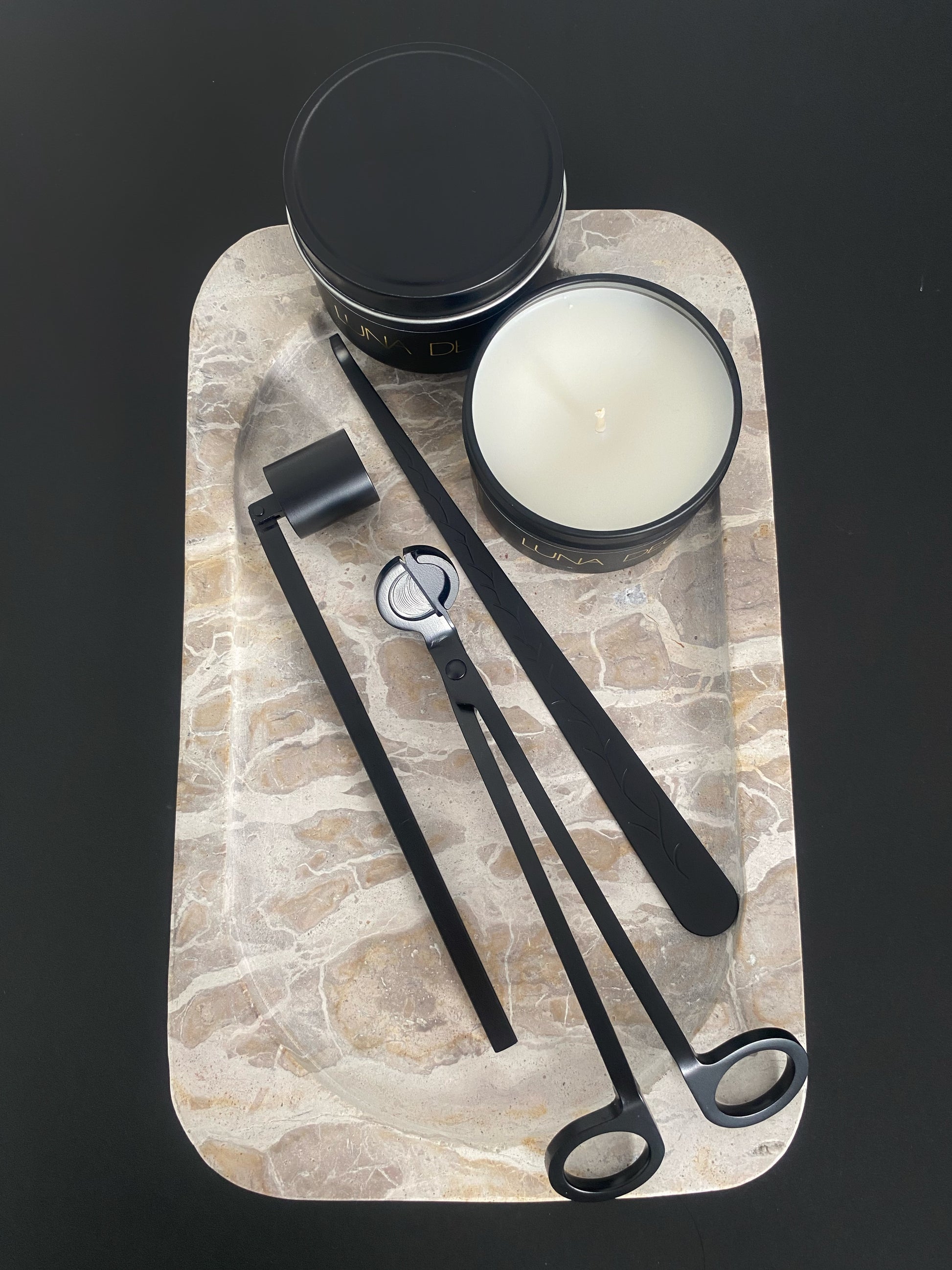 Candle and candle accessories tools on a stone tray with a black background including wick trimmer, candle snuffer and dipper. 
Candle essentials, candle accessories, 
must-have for every true candle lover - designed to enhance the longevity, beauty and ritual pf your candle. 
Luna Deco