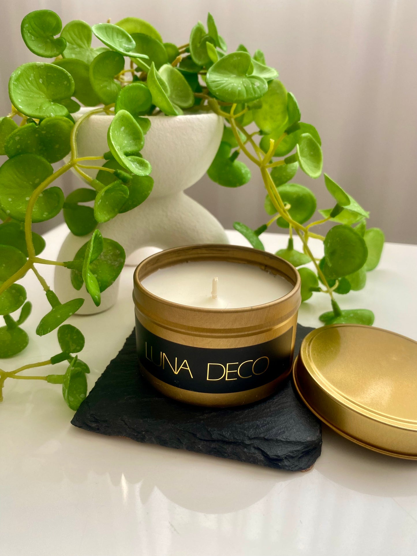 Luna Deco candle in a gold tin with a plant in the background.
Matte gold travel tin, perfect for travel, small spaces or thoughtful gifting.
Minimalist, timeless, elegant design, artisan-made candles. 
Luna Deco