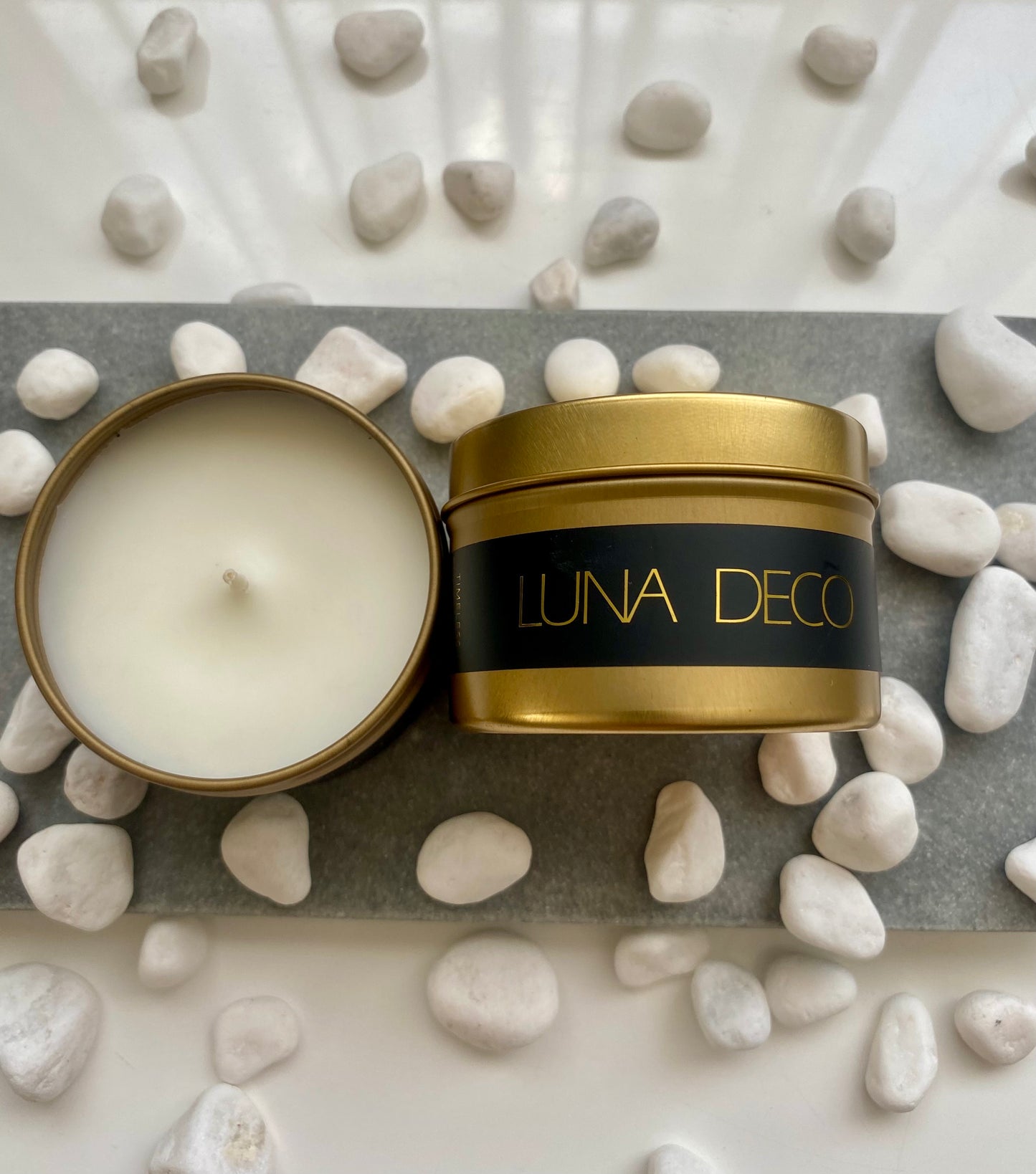 Luna Deco travel tin candle in a decorative setting with pebbles.
Matte gold travel tin candle,  perfect for travel, small spaces or thoughtful gifting.
Minimalist, timeless, elegant design, artisan-made candles. 
Luna Deco. 