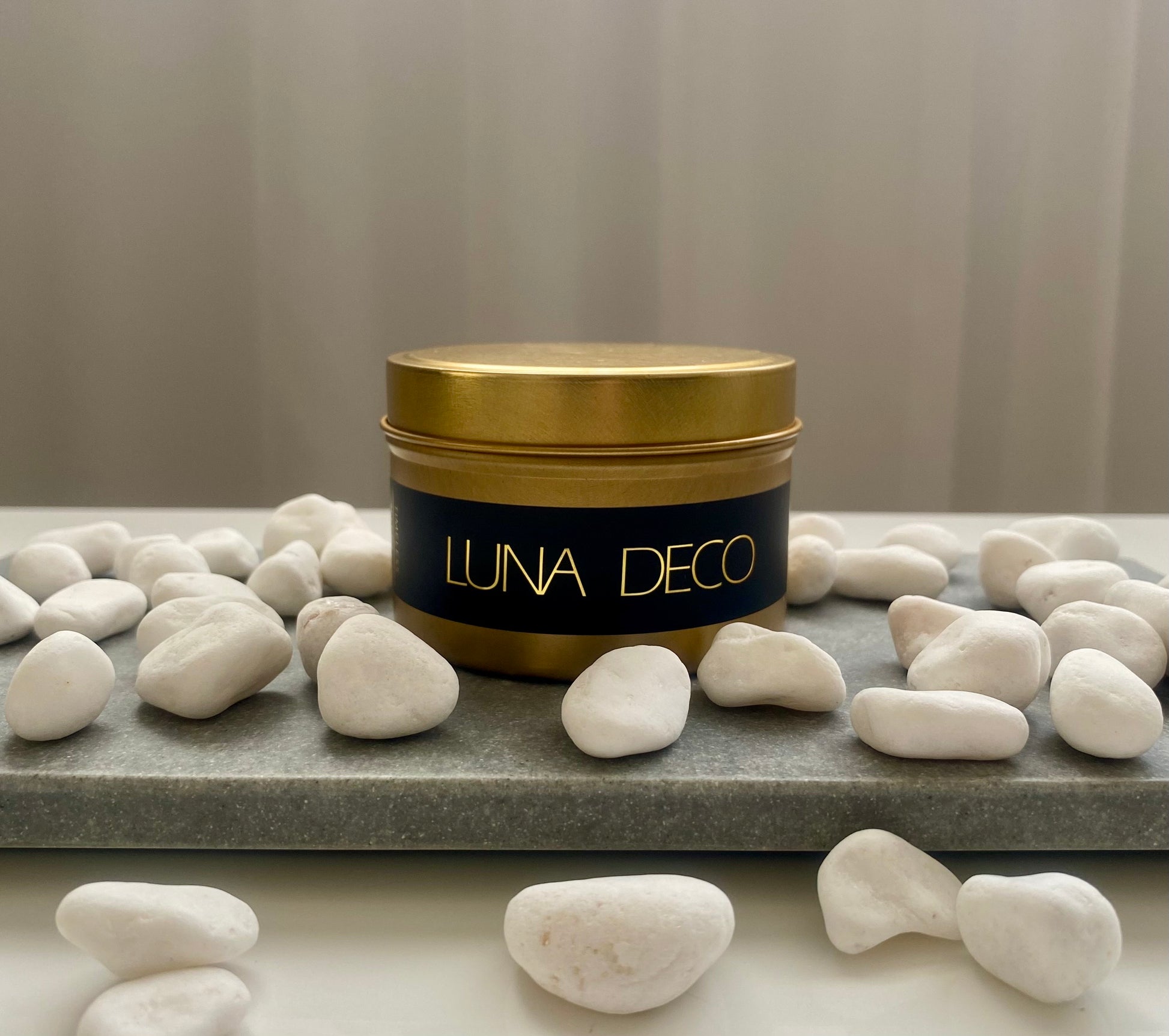 Luna Deco gold travel tin surrounded by white stones on a gray surface. 
Matte gold travel tin, perfect for travel, small spaces or thoughtful gifting.
Minimalist, timeless, elegant design, artisan-made candles. 
Luna Deco
