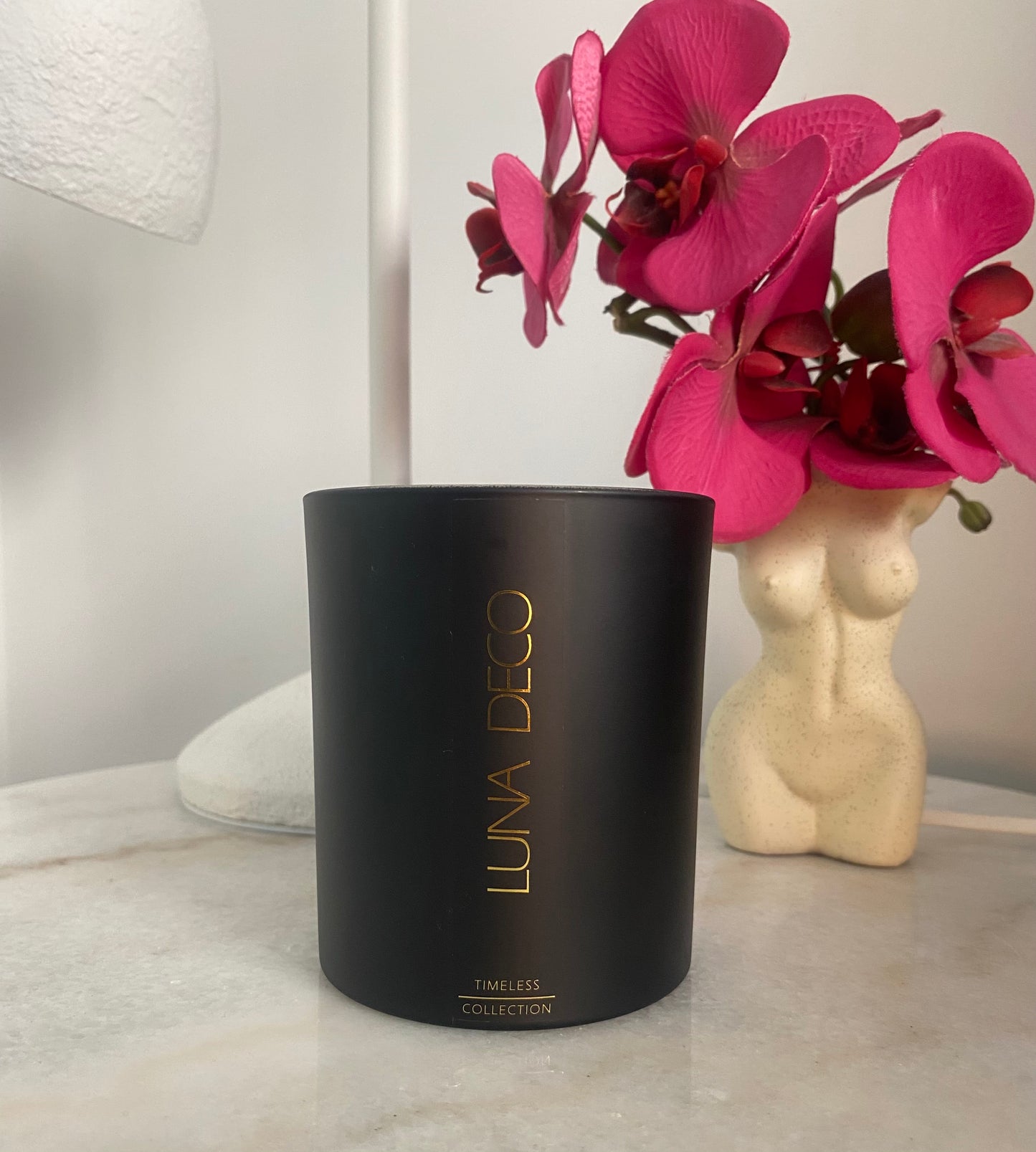 Black matte candle labeled 'LUNA DECO' on the bedside table with decorative flowers.
 Home decor ideas, minimalist style, Australian made soy candle, cozy home, home fragrance, calm and relax, hand-poured soy candles,clean and fresh burn, perfect gift, treat to yourself, stunning decoration piece, 