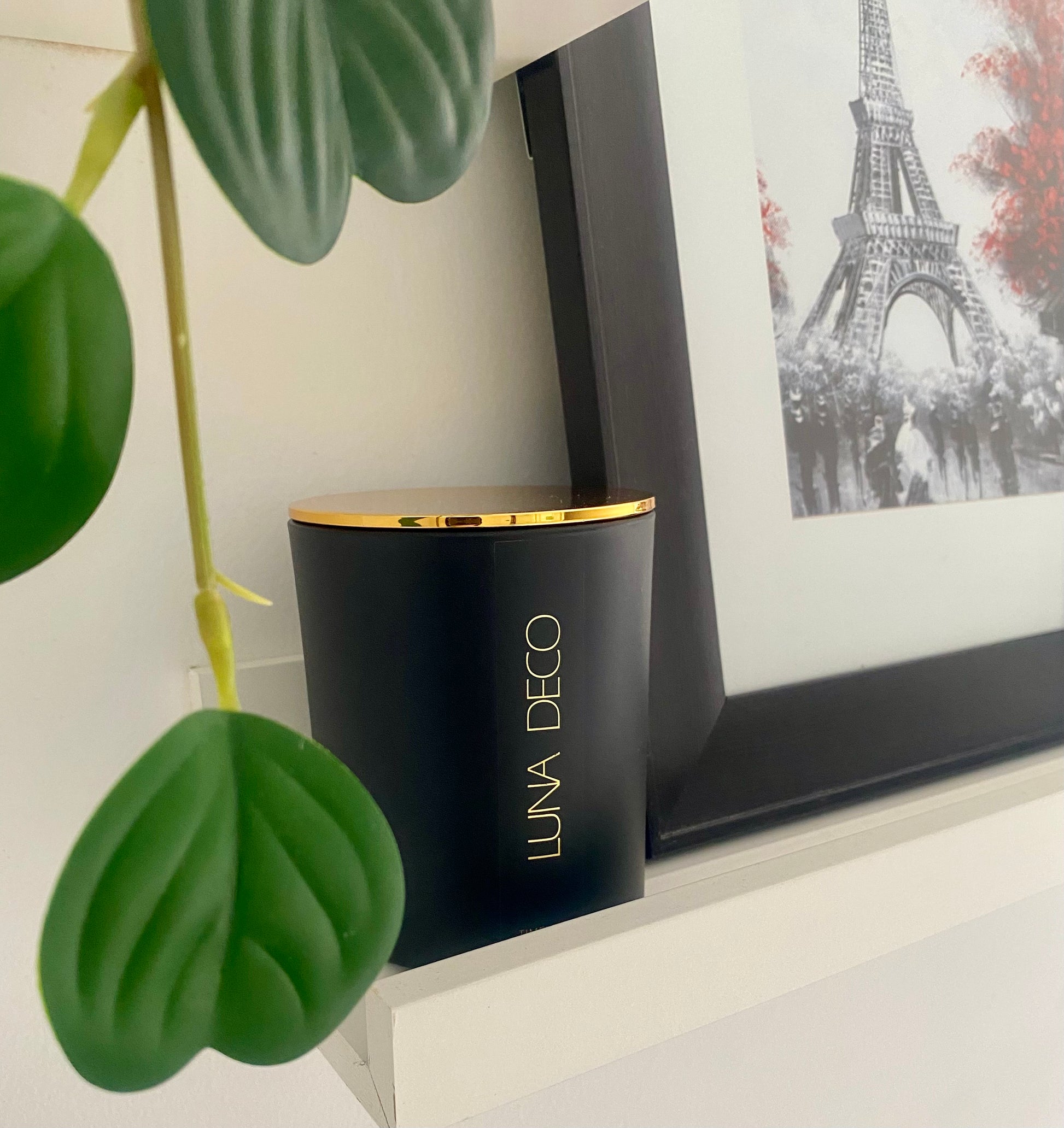 Black matte vessel with gold lid labeled 'LUNA DECO' next to a plant and framed picture of the Eiffel Tower.
Home decor ideas, minimalist style, Australian made soy candle, cozy home, home fragrance, calm and relax, hand-poured soy candles, clean and fresh burn, perfect gift, treat to yourself, stunning decoration piece, 